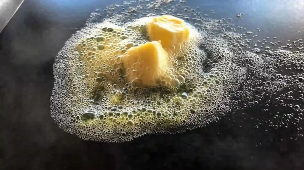 Butter melting and bubbling on a hot griddle before cooking morel mushrooms.